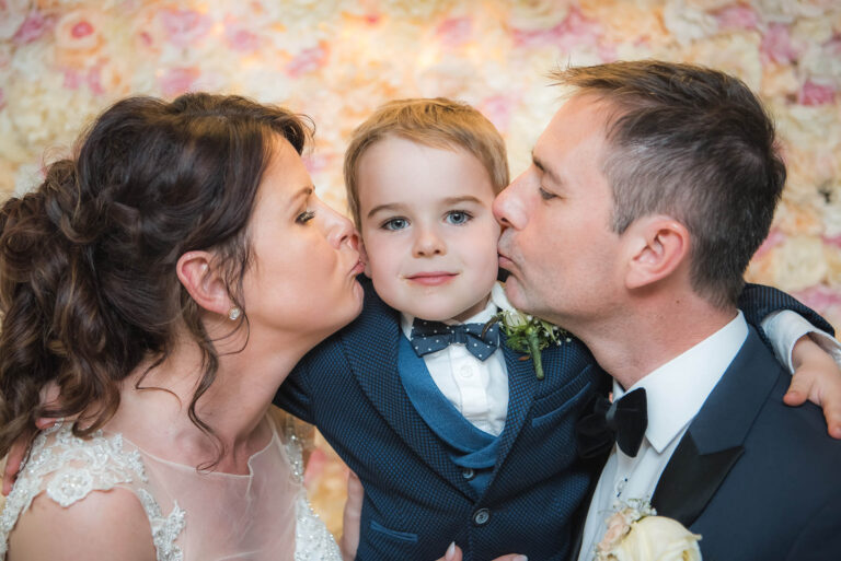 Beautiful bride and handsome groom smiling at each other during their wedding day while kissing their son