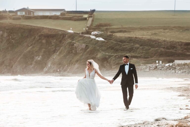 John and Sarah, newlyweds, holding hands during their beach wedding.